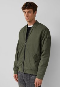 Olivenfarbene Bomberjacke aus leichtem Material. Sie verfügt über einen Reißverschluss vorne, gerippte Bündchen und zwei Seitentaschen.