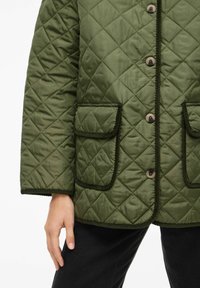 Veste matelassée verte à finition mate, dotée de grandes poches plaquées, d'une fermeture à boutons et d'un bord contrastant sur les contours.