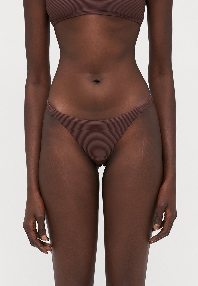 Brun stripete bikini-set som består av en bandeau-overdel og lavt skåret bunn. Stoffet har en jevn tekstur og minimalistiske designdetaljer.