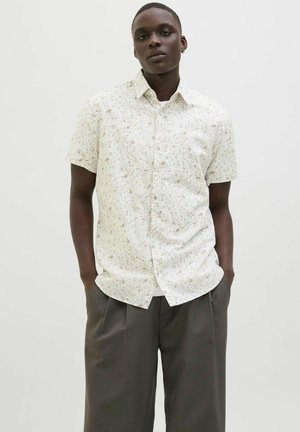 Camisa de manga corta con botones en beige claro con un diseño floral en tonos apagados de marrón y verde. La tela parece suave y tiene un corte relajado.