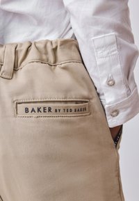 Beige trousers with an elastic waistband, featuring a label that reads "BAKER by TED BAKER." White collared shirt is partially visible.
