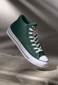 Sapatilha alta verde em lona, com atacadores brancos, sola em borracha e detalhes pretos ao longo da sola e da biqueira.