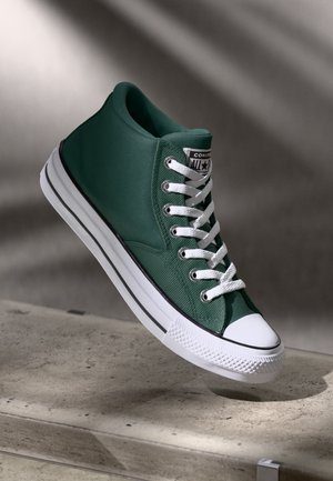 Zöld vászon magas szárú sneaker, fehér fűzőkkel, gumitalppal, és fekete részletekkel a talpon és az orrán.