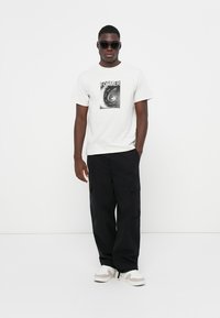 White t-shirt with a black graphic print reading "FORMER" on the front, paired with black cargo pants and white sneakers. Black sunglasses are worn.