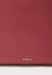 Czerwona skórzana torebka o fakturowanej powierzchni, z złotym logo "FURLA" na dole. Prosty design bez dodatkowych elementów czy ozdób.