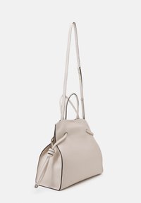 Ljusbeige läderhandväska med en strukturerad form, knutdetaljer på remmarna och svart kant längs kanterna. Justerbar axelrem.
