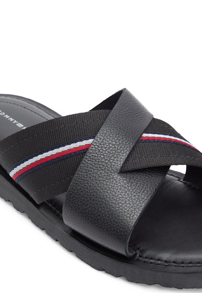 Sandalia tipo chancla negra con cuero texturizado y tiras tejidas con franjas rojas, blancas y azules, suela acolchonada y diseño de puntera abierta.