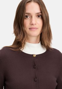 Dark brown cardigan made of soft fabric featuring a round neckline, heart-shaped gold button, and three matching round buttons.