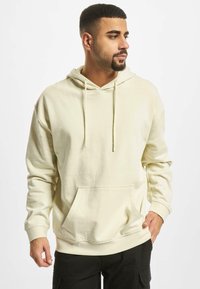 Cremefarvet hættejakke lavet af blødt stof, med en frontlomme i kangaroo-stil, snøre og ribbede manchetter. Casual og komfortabelt design.