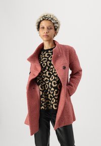 Casaco em mistura de lã cor-de-rosa com acabamento texturizado, apresentando um colarinho com corte clássico, botões pretos e bolsos, sobreposto a um suéter de padrão de leopardo.