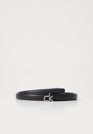 Zwarte gestructureerde leren riem opgerold met een kleine zilveren "ck" logo gesp tegen een witte achtergrond.