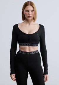 Μαύρο cropped τοπ με μακριά μανίκια και ριμπ υφή, με λαιμόκοψη με κουμπιά και αντίθετη ταινία με το λογότυπο "TOMMY JEANS" στο τελείωμα.