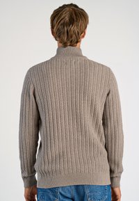 Grauer, gerippter Strickpullover mit hohem Kragen und langen Ärmeln. Verfügt über ein strukturiertes Muster und einen taillierten Saum. Wird mit blauen Denim-Jeans getragen.