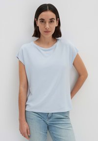 T-shirt azzurro chiaro a maniche corte realizzato in un tessuto morbido, con scollo rotondo, vestibilità rilassata e texture liscia. Indossato con jeans in denim chiaro.