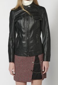 Czarna skórzana kurtka z kołnierzem typu stójka, przednim zamkiem błyskawicznym oraz dwoma zapinanymi na zamek kieszeniami. Teksturowane ramiona z prążkowymi detalami.