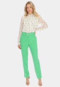 Biała bluzka w kropki z falbaną z przodu, zestawiona z jasnoszarymi, dopasowanymi spodniami. Całość uzupełniają beżowe szpilki i elegancki krój.