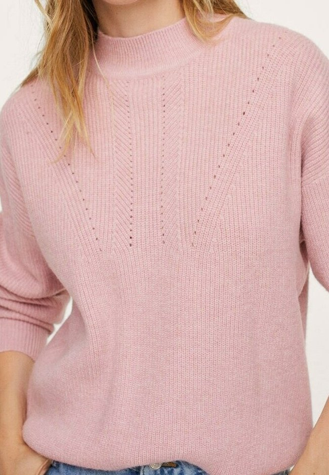 Femme portant un pull en maille rose clair avec de petits trous décoratifs en motif chevron et des manches retroussées.