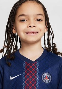 Temno modra nogometna majica z obliko V, ki ima geometrijski rdeč in modri vzorec, Nike logo ter okroglo značko PSG ekipe spredaj.