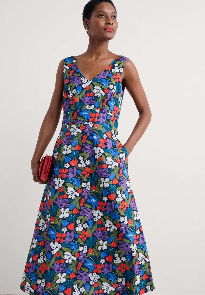 Rochie florală cu decolteu în V, fără mâneci și fustă evazată. Confectionată dintr-un material cu un model vibrant de flori roșii, albastre, mov și albe.