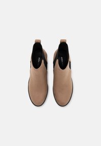 Botines bajos de ante color canela con un panel lateral elástico negro y una lengüeta para tirar. Textura suave y diseño de punta redonda, con una marca minimalista en el interior.