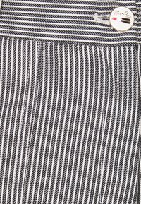Tessuto a righe bianche e nere con linee verticali, caratterizzato da un bottone in metallo accentuato in vita. La texture è liscia con cuciture a contrasto.
