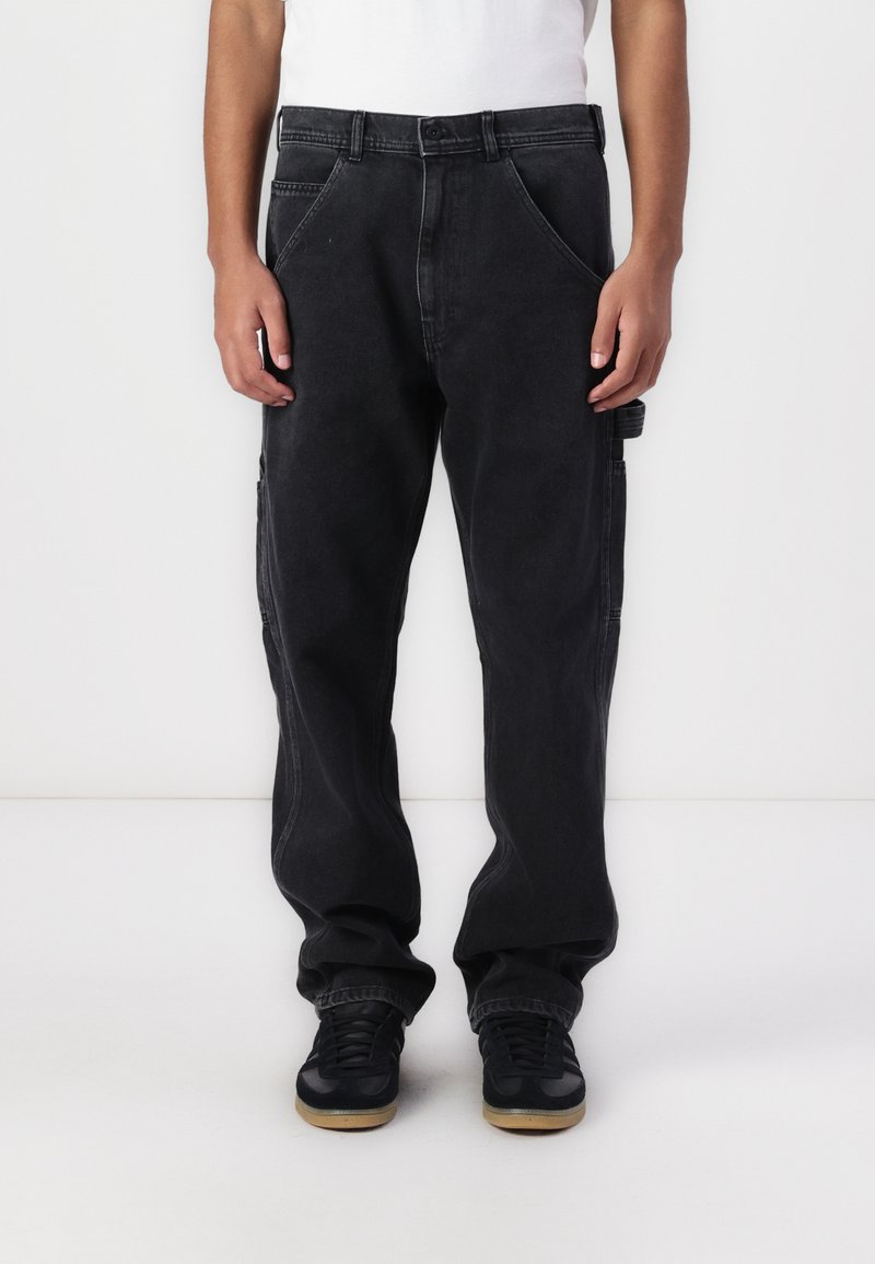 Black denim cargo pants with loose fit, diagonal front pockets, and side pockets. Features a button closure and visible stitching accents.