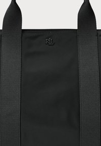 Črn toten nahrbtnik z gladkim blago telesom, trdnimi spletenimi naramnicami in subtilnim embosiranim logotipom. Preprost in funkcionalen dizajn z zadrgo.