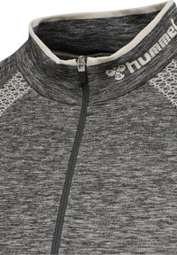 Cazadora deportiva gris con textura, de cremallera con alto collar y ribete blanco en contraste. Presenta una cremallera de un cuarto y detalles de malla.