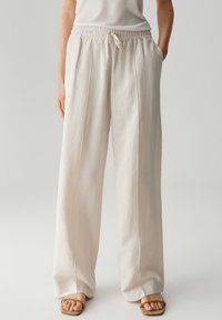 Lichte beige culotte met een elastische tailleband, een trekkoord en zijzakken; gladde textuur en geplooide naden aan de voorkant.
