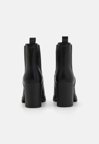 Černé kožené kotníkové boty s hladkým povrchem, blokovými podpatky a elastickými bočními panely pro snadné obouvání. Jednoduchý, elegantní design.