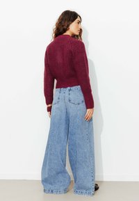 Pull en tricot côtelé bordeaux à manches longues, associé à un jean large bleu clair, avec une taille haute et une coupe décontractée.