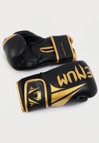 Μαύρα γάντια πυγμαχίας με χρυσές λεπτομέρειες, με απαλή υφή, επενδυμένα κόκαλα στα δάχτυλα και λογότυπο στο λουράκι στον καρπό. Ρυθμιζόμενο κλείσιμο με βέλκρο.