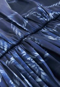 Gros plan sur un tissu bleu foncé avec des motifs de feuilles blanches et des plis froncés créant des plis texturés.