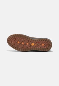 Suela de goma marrón con surcos profundos, con un logotipo circular naranja y una superficie texturizada; resistente y diseñada para ofrecer tracción.