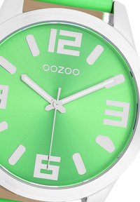 Green dial watch with bold white numerals, silver casing, and a green silicone strap. Features simple, clean design and minimalist hands.