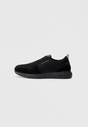 Black suede sneakers with a textured finish, contrasting rubber sole, and subtle branding on the side. Features a pull-tab at the heel.