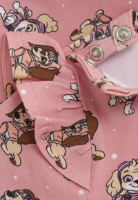 Rosa Stoff mit einem sich wiederholenden Cartoon-Hundemuster, kleinen weißen Punkten und Druckknöpfen auf der linken Seite. Weiche Textur mit Rüschendetail.