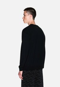 Maglione nero in un morbido tessuto lavorato a maglia, con scollo rotondo, maniche lunghe e design minimalista con una piccola etichetta sul retro.