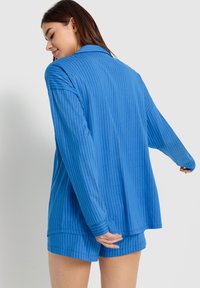 Blårandig långärmad topp och matchande shorts, tillverkade av ett mjukt material med en avslappnad passform. Har krage och manschetter, med vertikala ränder.