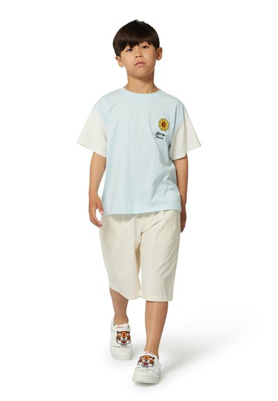 T-shirt bleu clair avec des manches blanches, broderie de tournesol ; shorts crème ; baskets blanches avec un design de tigre.