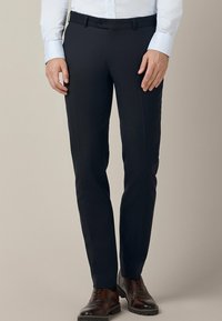 Granatowe spodnie garniturowe o dopasowanym kroju, gładkim przodzie i szlufkach na pasek, wykonane z gładkiego, tkanej tkaniny. W połączeniu z brązowymi skórzanymi butami.