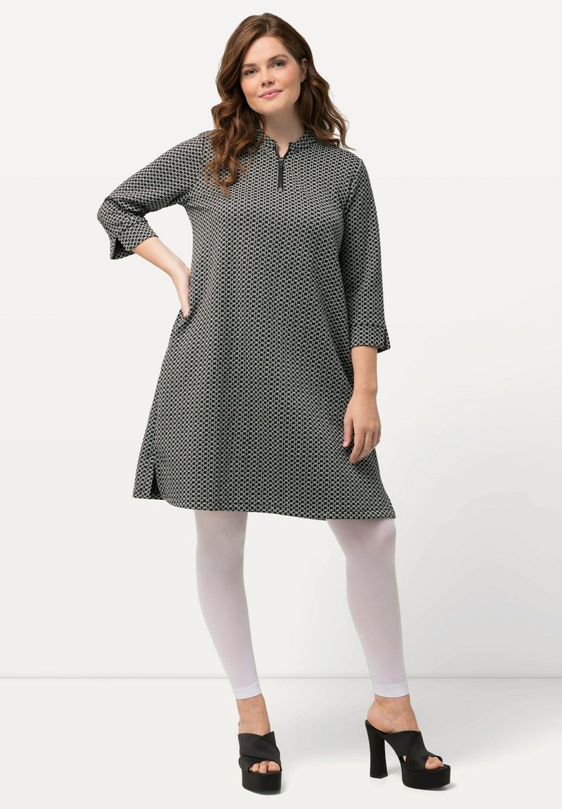 Abito con motivo in bianco e nero, dal collo alto e maniche tre quarti, abbinato a leggings bianchi e sandali con zeppa neri.