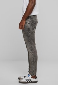 Jeans ajustados de corte desvaído en gris con pierna entallada. Presenta dos bolsillos traseros y detalles de costura sutil. Llevados con zapatillas blancas y grises.