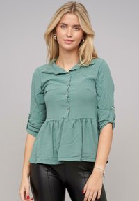 Top peplum verde acqua con bottone in tessuto leggero, colletto, maniche arrotolate e vita arricciata per una vestibilità comoda.