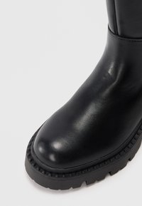 Black leather ankle boot with a smooth finish, rounded toe, and textured rubber sole featuring a slight tread pattern.