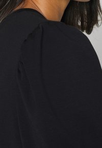 Black puff sleeve top made of soft fabric, featuring subtle gathers at the shoulders for added texture and a smooth finish.