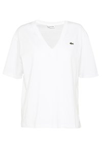 Vit kortärmad V-ringad tröja med en liten grön krokodil-logotyp på vänster bröst, tillverkad av lätt material.