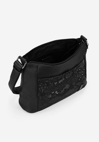 Bolso cruzado de cuero negro con panel de textura en relieve, cierre con cremallera y correa ajustable. El interior está forrado en tela negra.