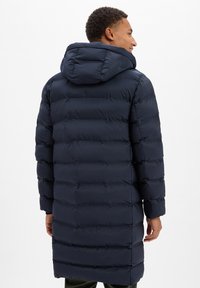 Granatowa pikowana kurtka puchowa z kapturem, z pionowym przeszyciem, długim krojem i elastycznymi mankietami. Miękka, ocieplana tkanina.