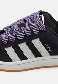 Černá semišová teniska s bílým designem tří pruhů a fialovými tkaničkami ve tvaru cikcak. Má texturovanou bílou podrážku a nápis "CAMPUS".